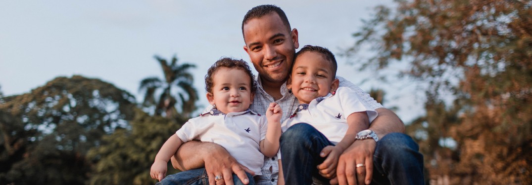 A father holding onto his two young kids while smiling.