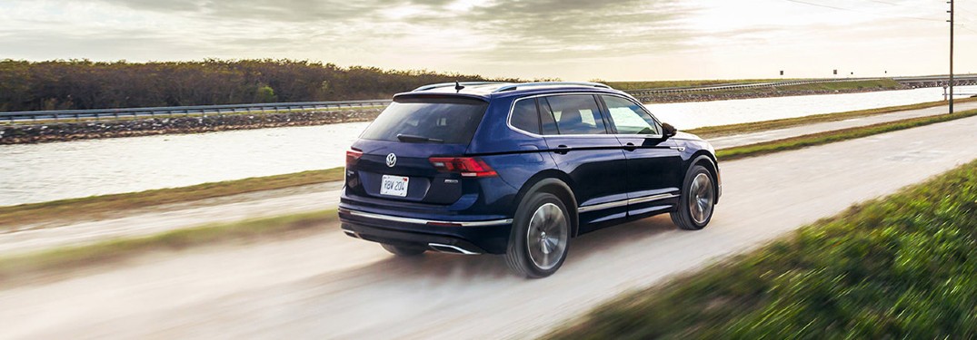 The rear and side view of a dark blue 2021 Volkswagen Tiguan driving down an empty road.