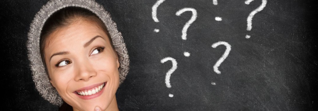 A young woman looking at a chalkboard with question marks written on it.