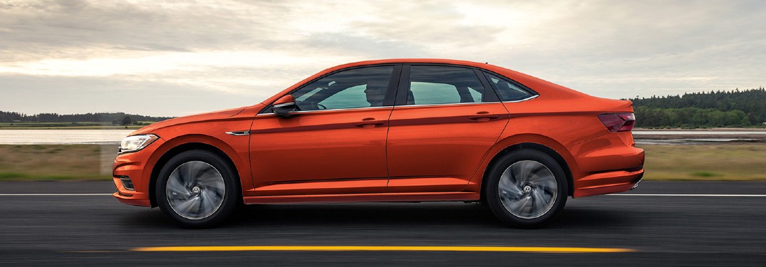 The side view of an orange 2021 Volkswagen Jetta driving down a road.