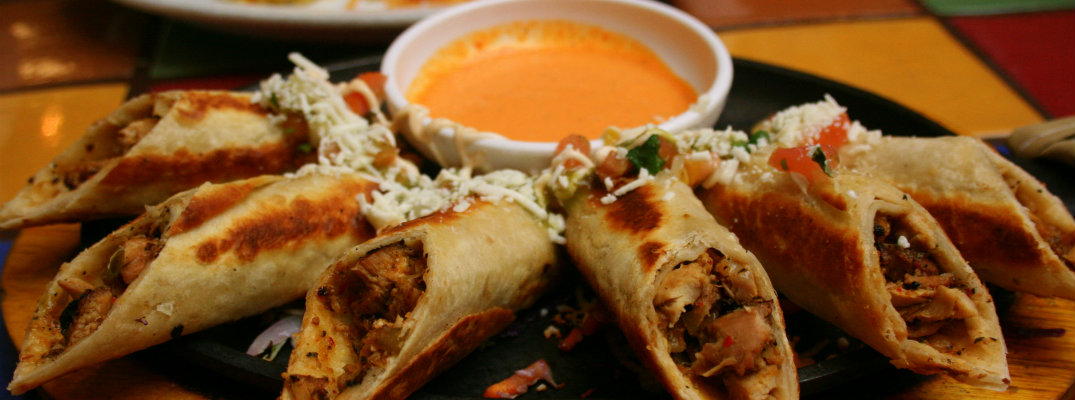 a plate tray of rolled chicken tacos with cheese dipping sauce at a mexican restaurant for cinco de mayo