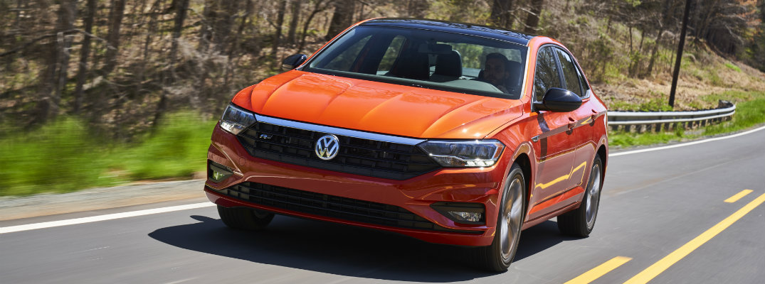 2019 Volkswagen Jetta R-Line trim level exterior orange paint driving on a road near a barren forest