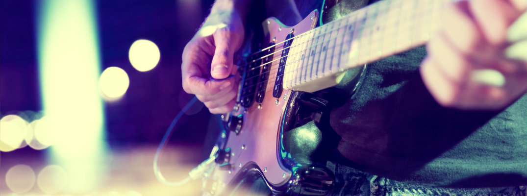 close up of a man strumming and playing an electric guitar on stage