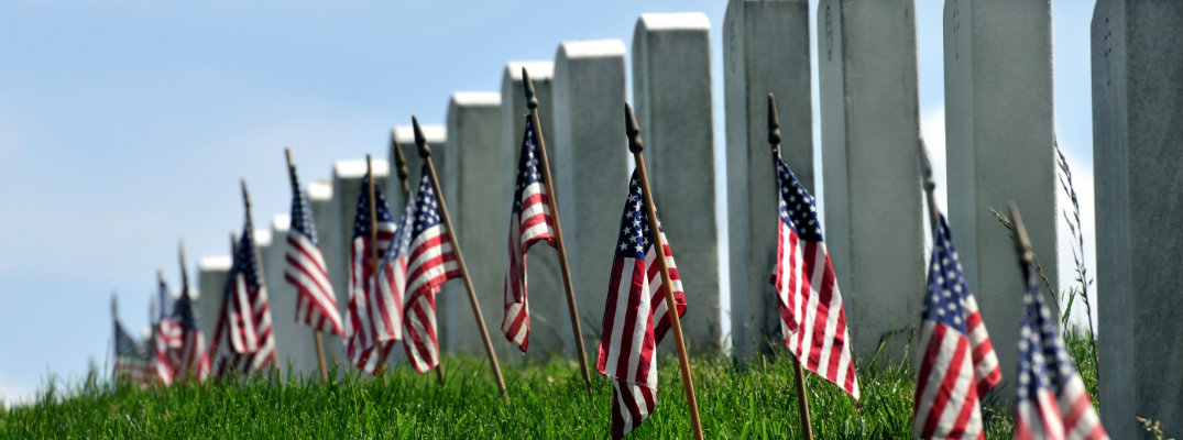 American flags planted in the grass ground next to a line of gravestones for soldiers on Memorial Day
