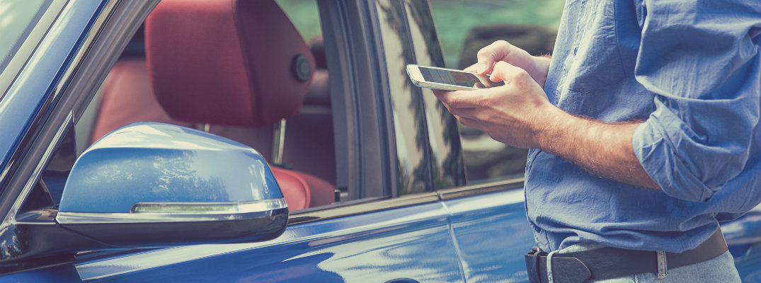 a man checking his smartphone right outside the driver's door to his blue car