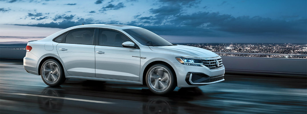 2020 Volkswagen Passat exterior shot with white paint color driving down a wet highway at night with a lit up city and clouds in the background