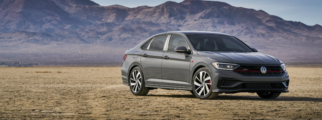 2019 Volkswagen Jetta GLI exterior shot with dark gray metallic paint color parked in a desert with a mountain range far behind it