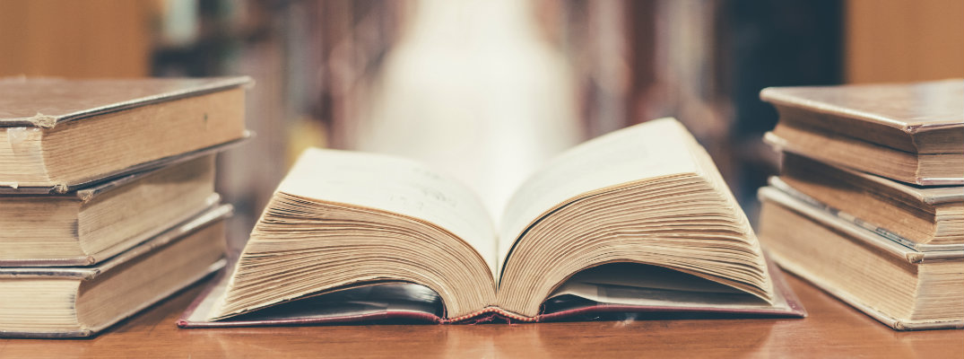 an old and worn book lying open on its spine with piles and aisles of books beside it in a library bookstore