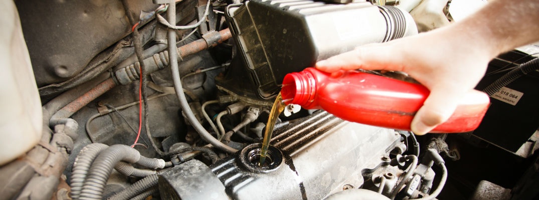 A stock photo of a hand pouring fresh motor oil into an engine