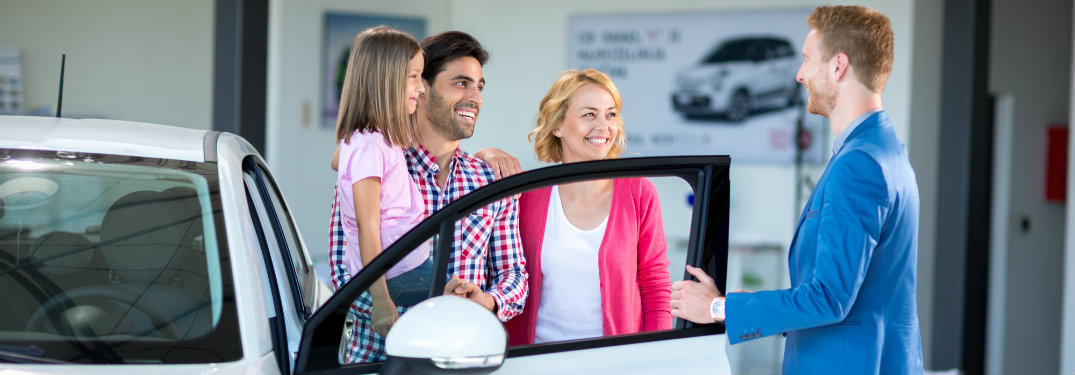 family-and-salesman-standing-next-to-new-car-in-dealership-showroom