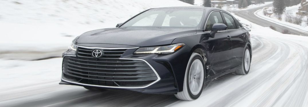 Driver's side front angle view of dark blue 2020 Toyota Avalon driving on a snowy road