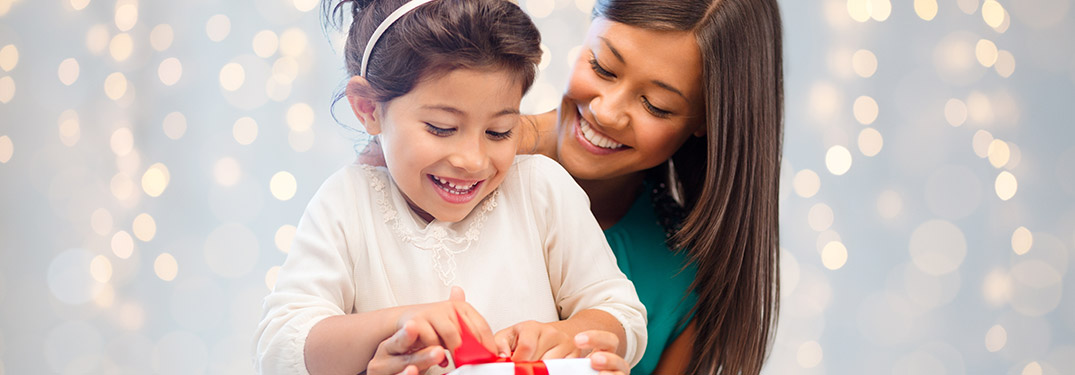 mother holding daughter while she opens present