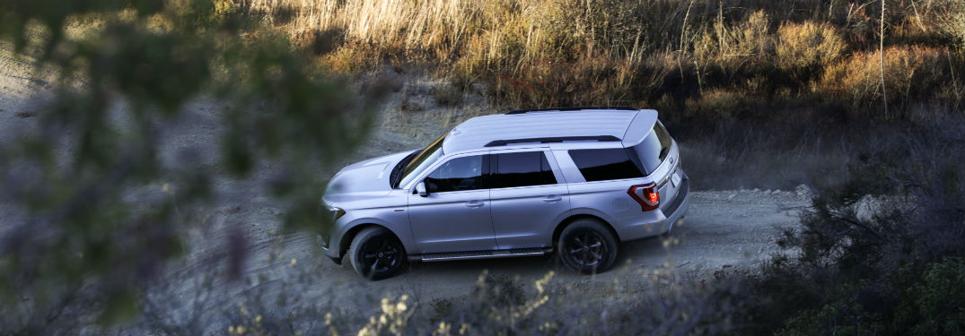 side view of a silver 2018 Ford Expedition driving along a tree-lined dirt road