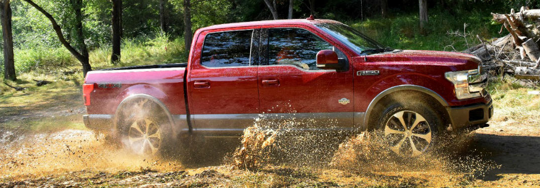 side view of a red 2018 Ford F-150 driving through a muddy puddle