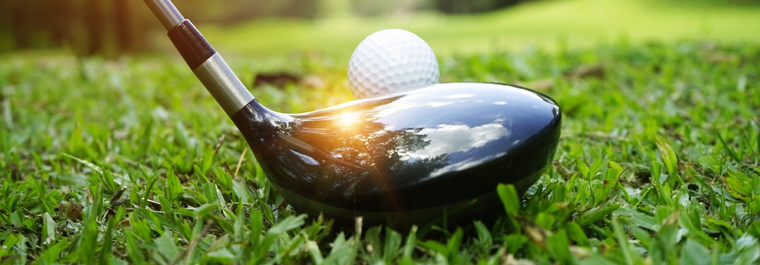 a golf club set up to a golf tee and golf club on the green and the sun reflects off of it