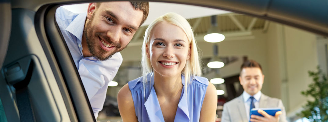 A stock photo of a young couple looking at buying a new car.