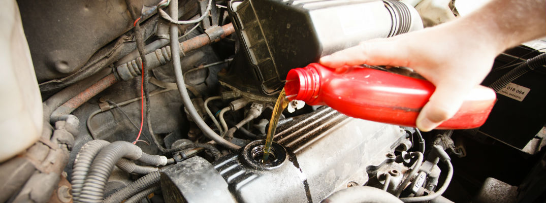 A stock photo of a person pouring oil into a car's engine.