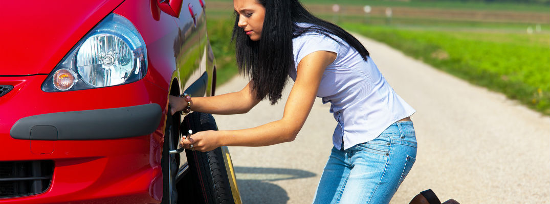 A stock photo of a young woman changing a tire.