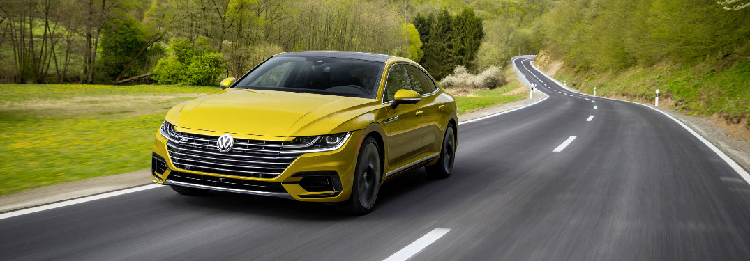 2019 Volkswagen Arteon in bright yellow driving along an empty stretch of road