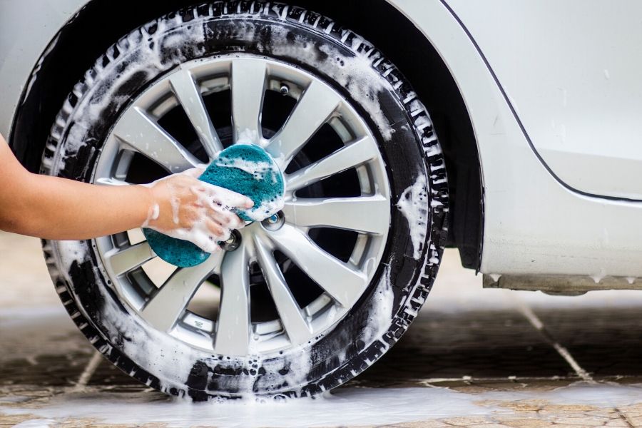 Hand holding sponge and cleaning car wheels with soap