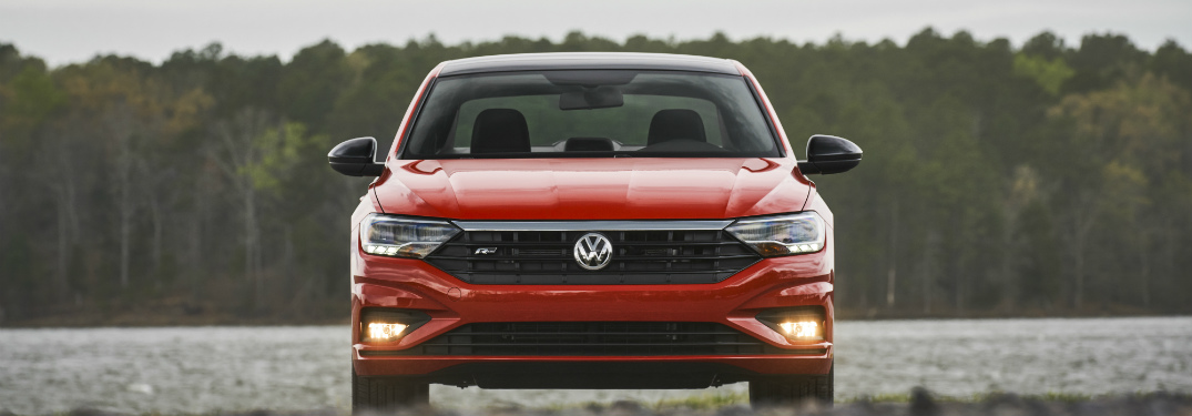 front bumper and grille of orange 2019 volkswagen jetta with a lake and trees behind it