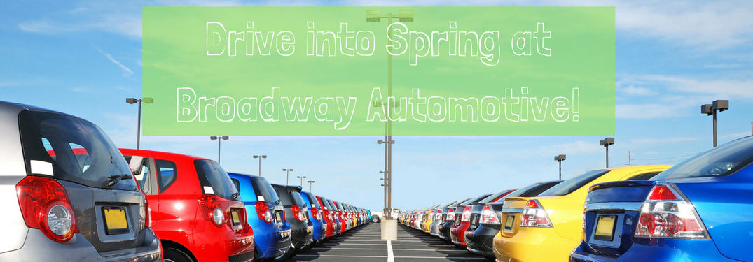 cars on car dealership lot with text "drive into spring at broadway automotive" above it