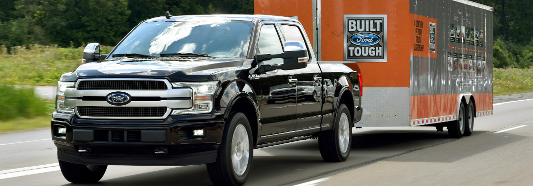black 2018 ford f-150 towing orange ford trailer on highway