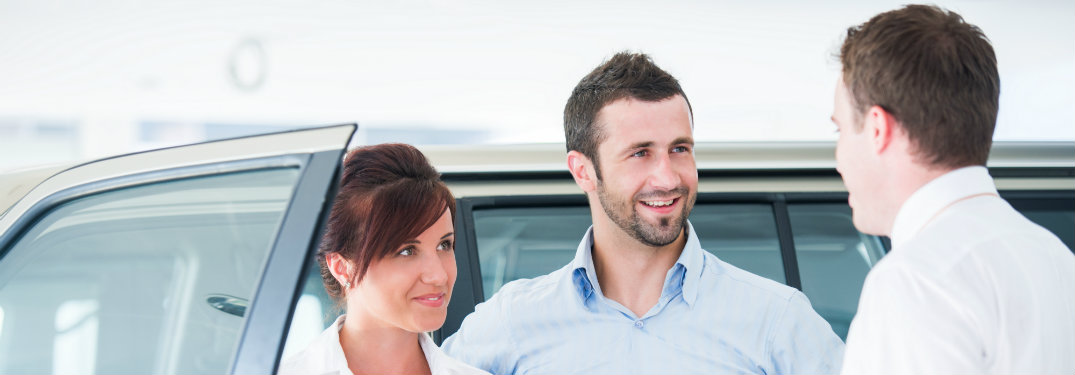 couple speaking to car sales person while looking at a vehicle