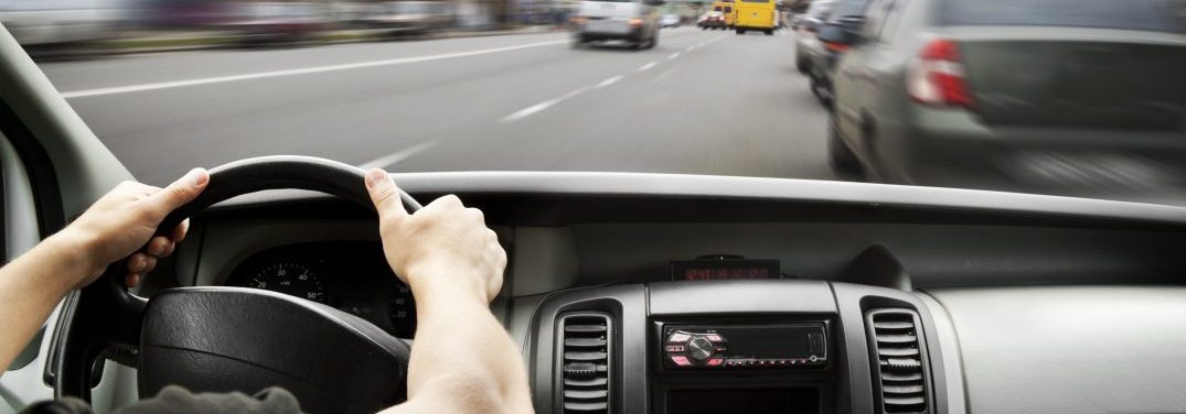 Man's hands of a driver on steering wheel of a minivan car on asphalt road