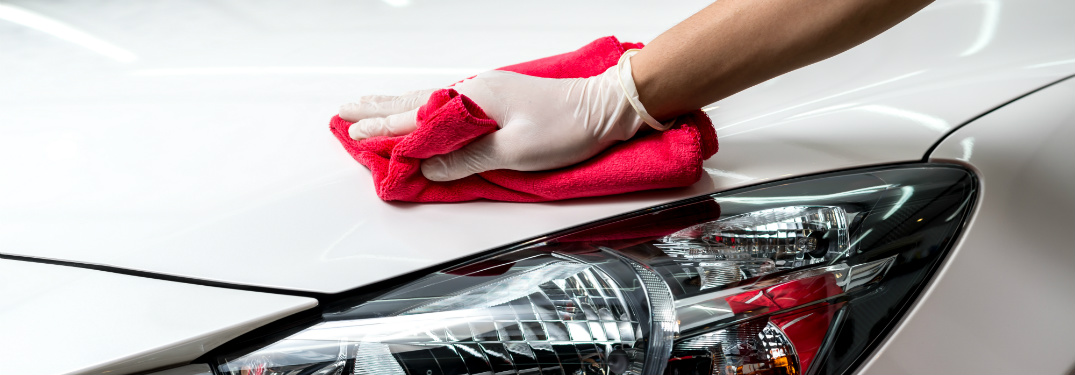 person cleaning exterior of white car with red cloth
