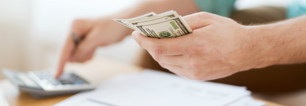a man's hands counting dollar bills while using calculator
