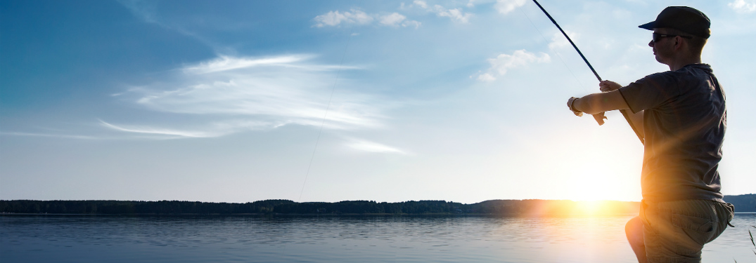 man fishing on lake with rod and sun behind him