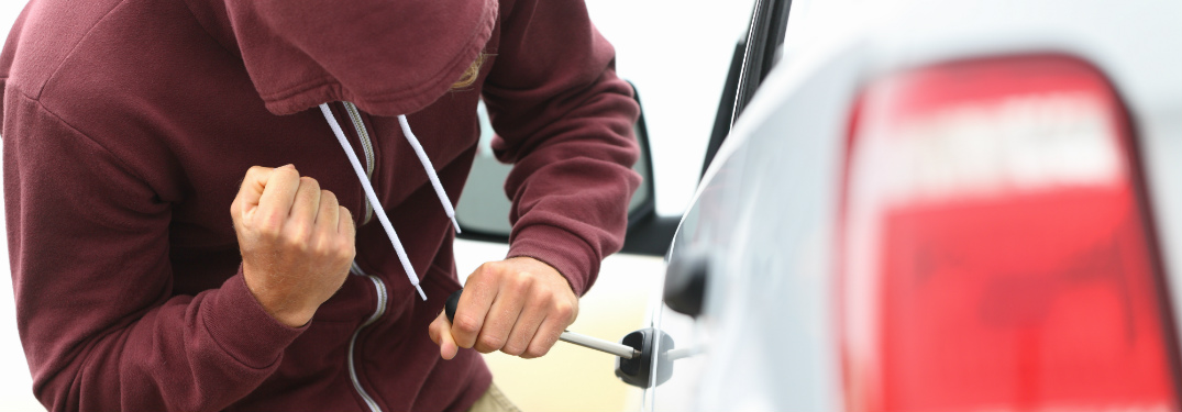 man in hood leaning over car door handle and trying to break in