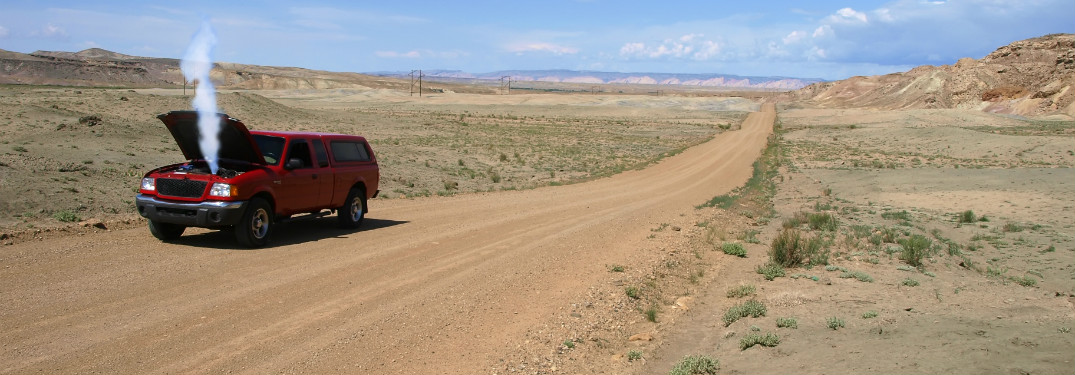 red suv on side of dirt road in empty desert with hood up and smoke coming out