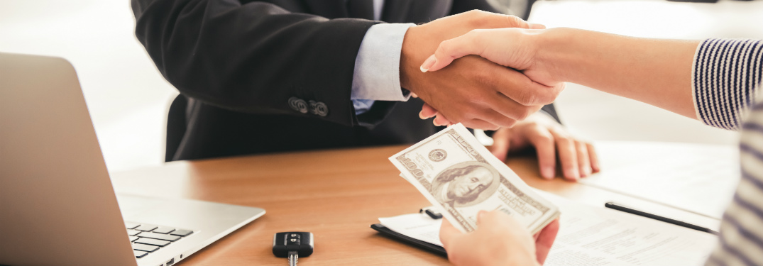 woman shaking hand of salesman while holding money in other hand