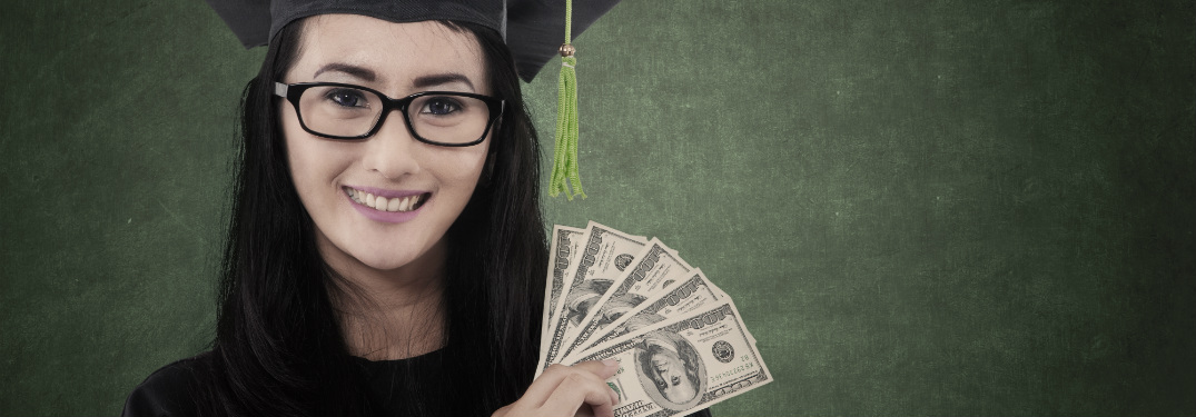 young woman in cap and gown holding cash dollar bills