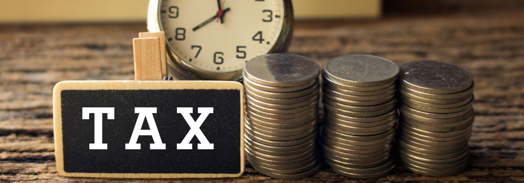 wooden block with "tax" written on it next to stack of coins and clock