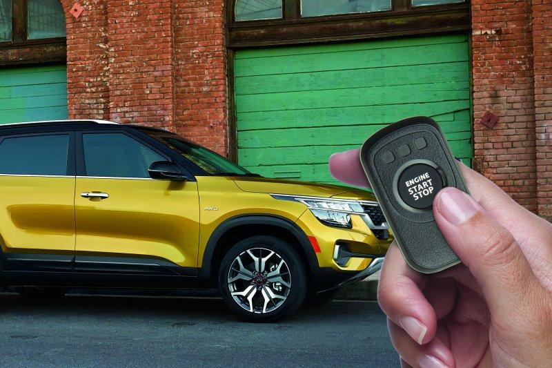 Hand holding remote start fob in front of yellow 2021 Kia Seltos