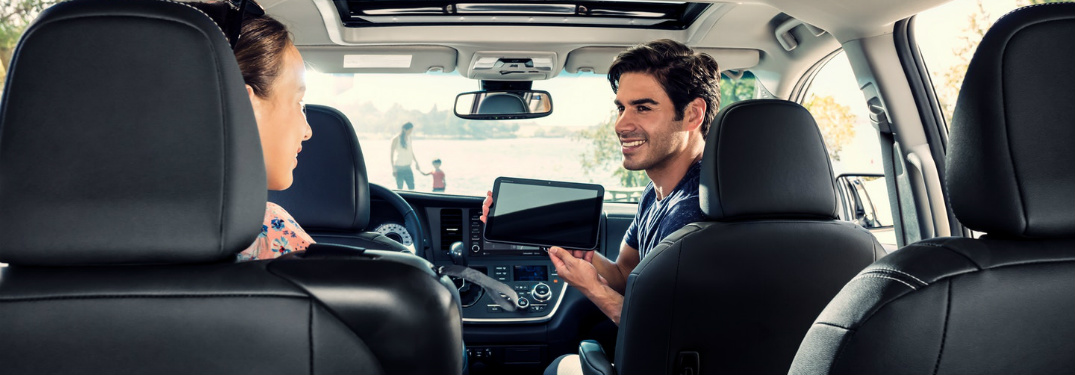 man in front seat of minivan turning around to show someone a tablet
