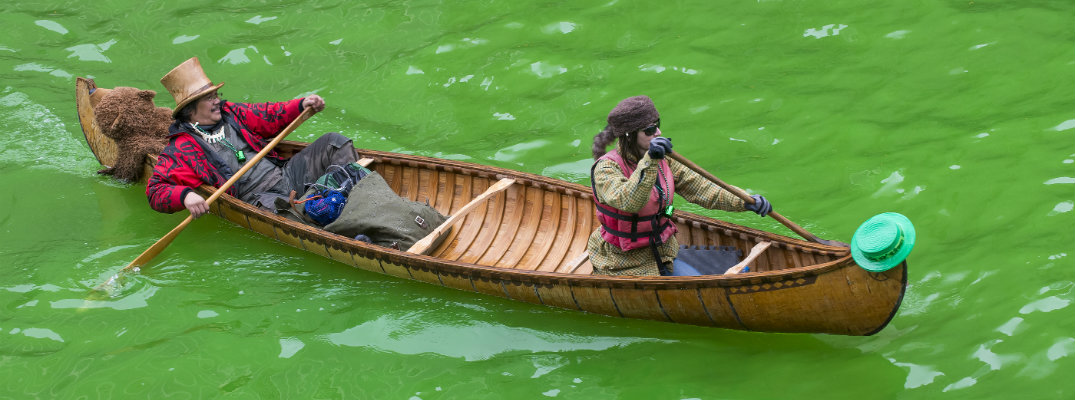 2 people canoeing in costumes down the green dyed Chicago River on St. Patrick's Day