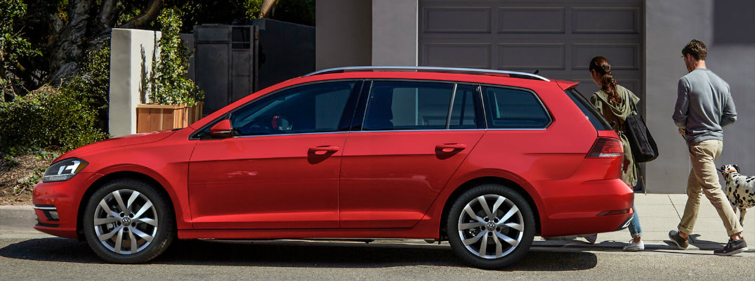 2018 Volkswagen Golf SportWagen red exterior side shot parked in front of a house garage as a couple and their dog walk past it