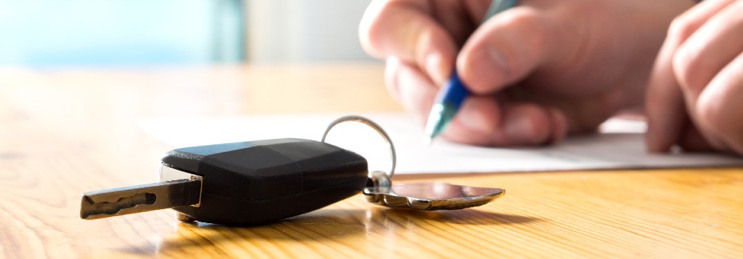 someone signing paper with keys near it