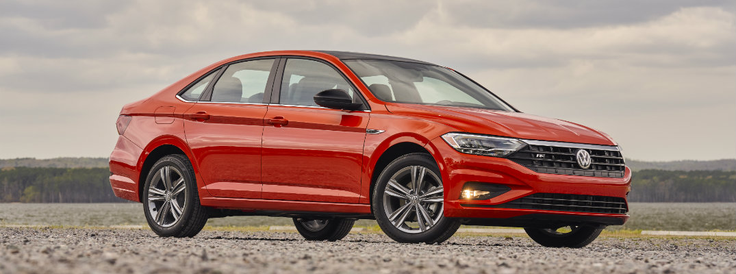 2019 Volkswagen Jetta R-Line trim level exterior shot parked on rocky ground wilderness with a forest and cloudy sky in the background habanero orange metallic color