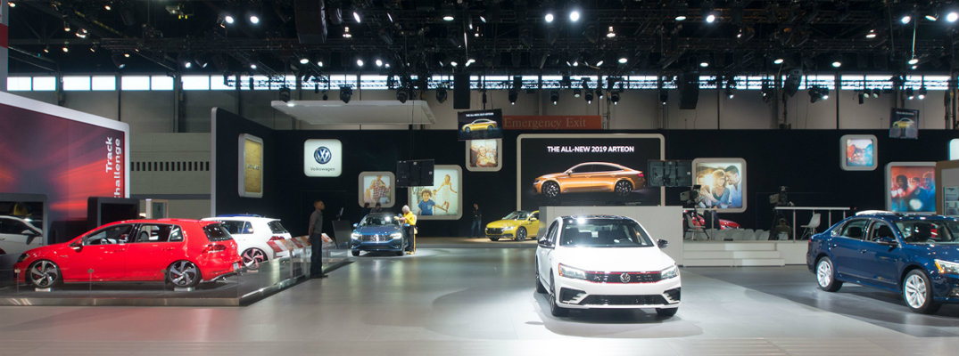 Volkswagen Auto Show display floor with screens, signs, and VW models such as the Golf, Passat, Jetta, and more