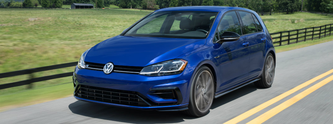 2018 Volkswagen Golf R exterior shot blue driving down a country highway next to a grassy field and wooden fence