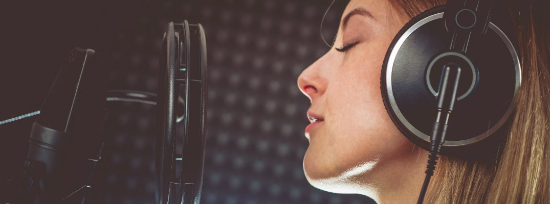 woman in a sound recording room singing into a microphone with her headphones on