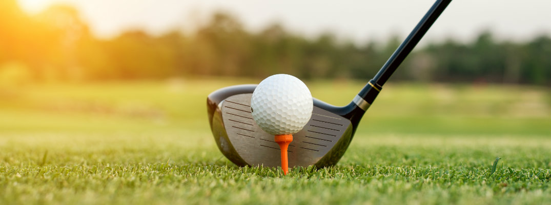 golf club behind a golf ball on a tee on the green with a shining sun in the background