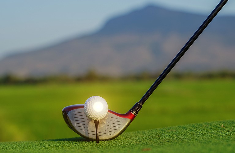 Photo of tee, ball and driver in front of mountian