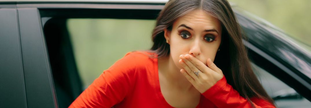 A lady in red top is feeling nauseated while on the road in a car.