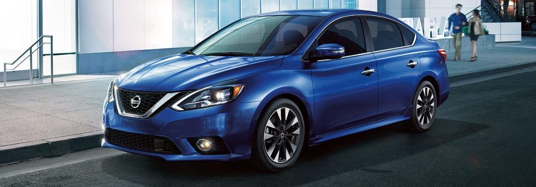 Blue 2018 Nissan Sentra parked in front of a modern building with two people walking toward it